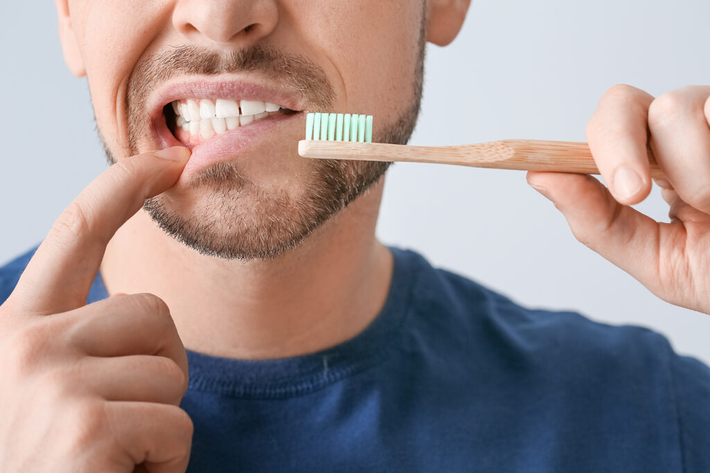 Man Pointing to His Gums While Holding a Toothbrush